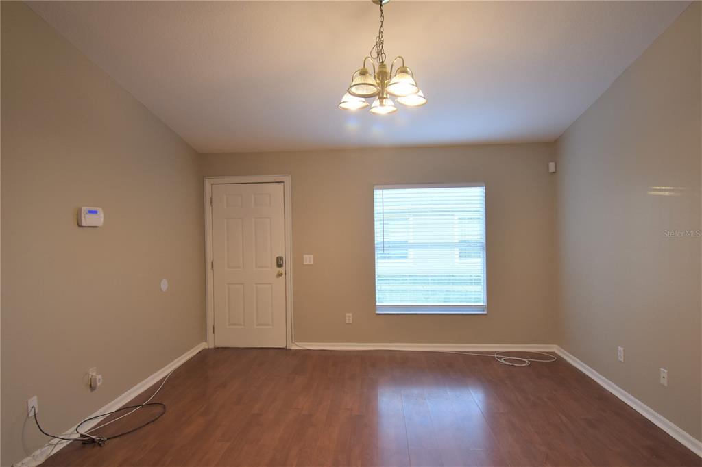 An empty room features wood-look flooring, beige walls, a chandelier, a window, and a door — 4406 E MANGO TERRACE, TAMPA, FL