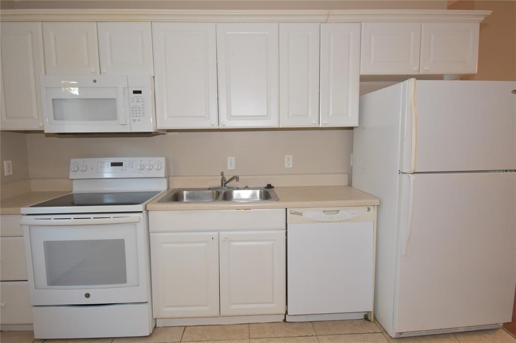 A kitchen features white cabinets, white appliances, a double sink, and beige countertops — 4406 E MANGO TERRACE, TAMPA, FL