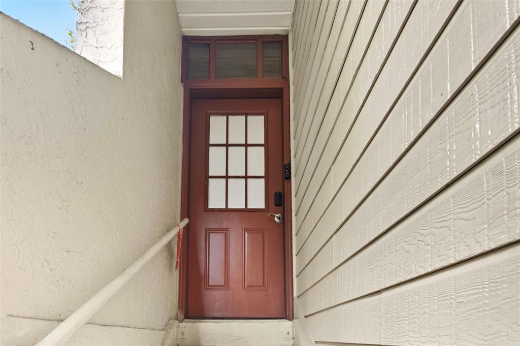 A red door with a glass window pane sits at the top of outdoor stairs — 2936 S SEMORAN BOULEVARD UNIT 106, ORLANDO, FL