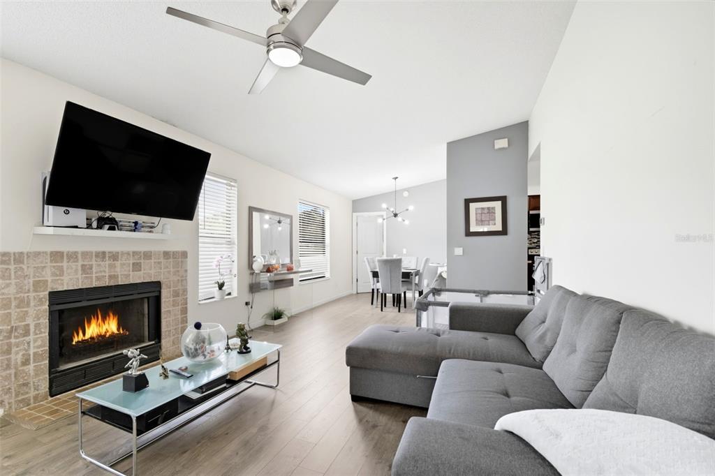 A living room with a fireplace, gray sectional sofa, and an adjacent dining area — 2936 S SEMORAN BOULEVARD UNIT 106, ORLANDO, FL