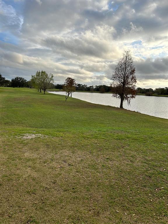 A grassy lawn slopes down toward a lake under a cloudy sky with several trees — 1014 JAPONICA DRIVE, INDIAN LAKE ESTATES, FL