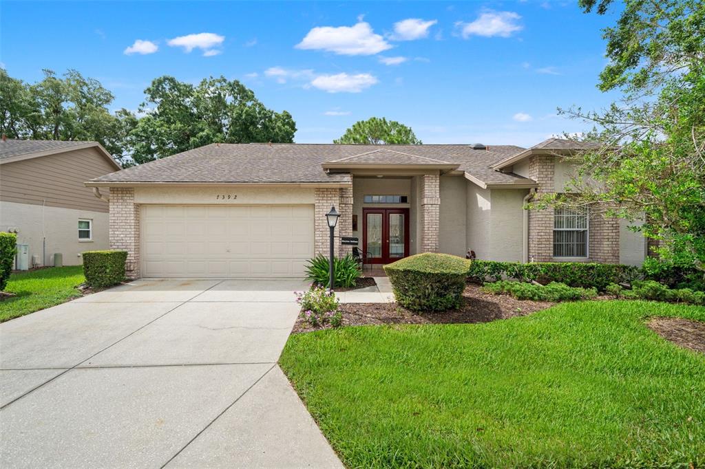 A single-story house with a beige stucco exterior, brick accents, and a two-car garage — 7392 MEADOW BROOK LANE, SPRING HILL, FL