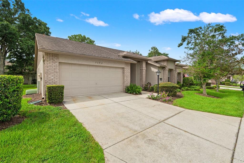 A single-story house with a beige garage, brick accents, and a concrete driveway — 7392 MEADOW BROOK LANE, SPRING HILL, FL
