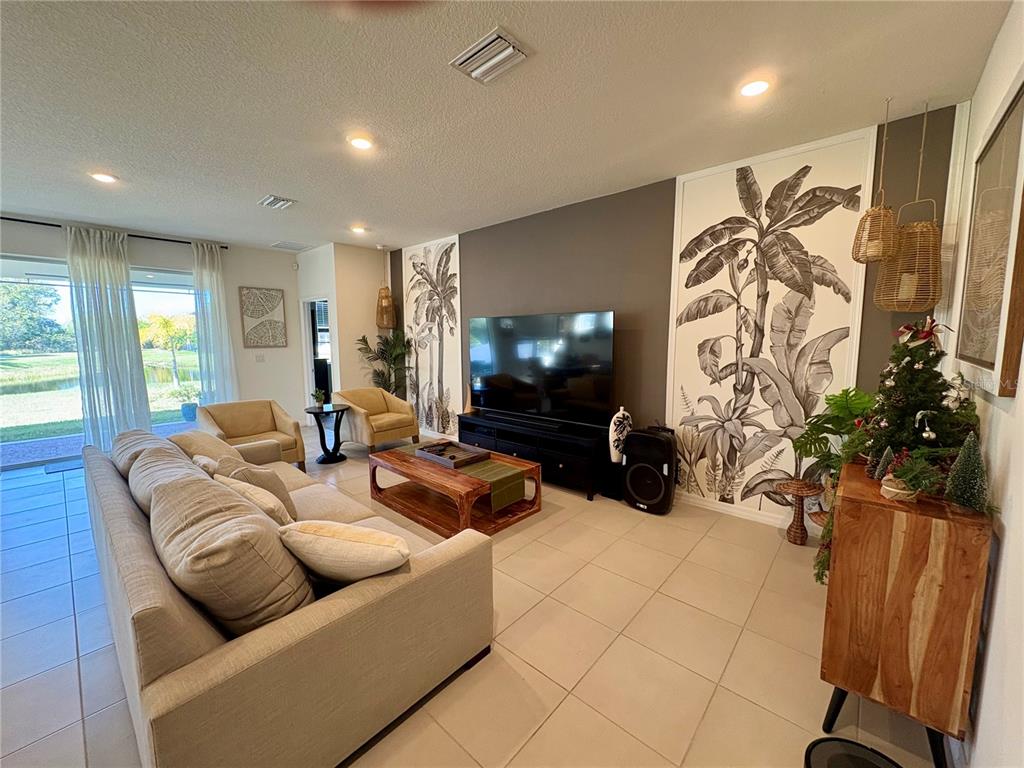 A living room features a large television, botanical wallpaper panels, and a beige sectional sofa — 13329 WATERLEAF GARDEN CIRCLE, RIVERVIEW, FL