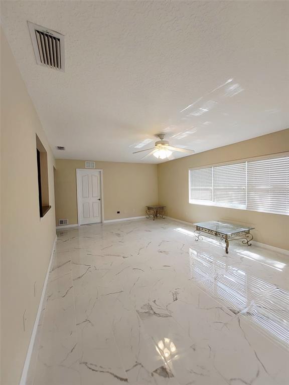 A bright, empty living room features white marble-look tile flooring, a ceiling fan, and blinds — 1102 NE 21ST TERRACE, OCALA, FL