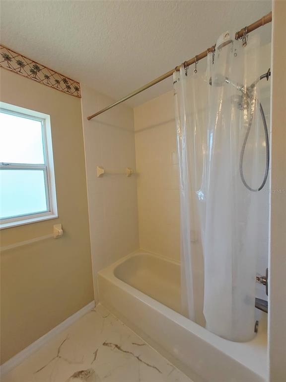 A bathroom features a white bathtub with a shower curtain, a window, and tiled flooring — 1102 NE 21ST TERRACE, OCALA, FL