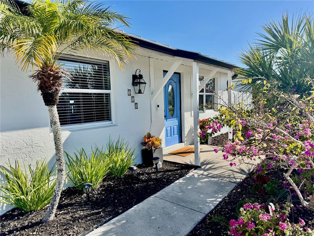 A white house exterior features a blue front door, a palm tree, and blooming bougainvillea — 118 ROTONDA CIRCLE, ROTONDA WEST, FL