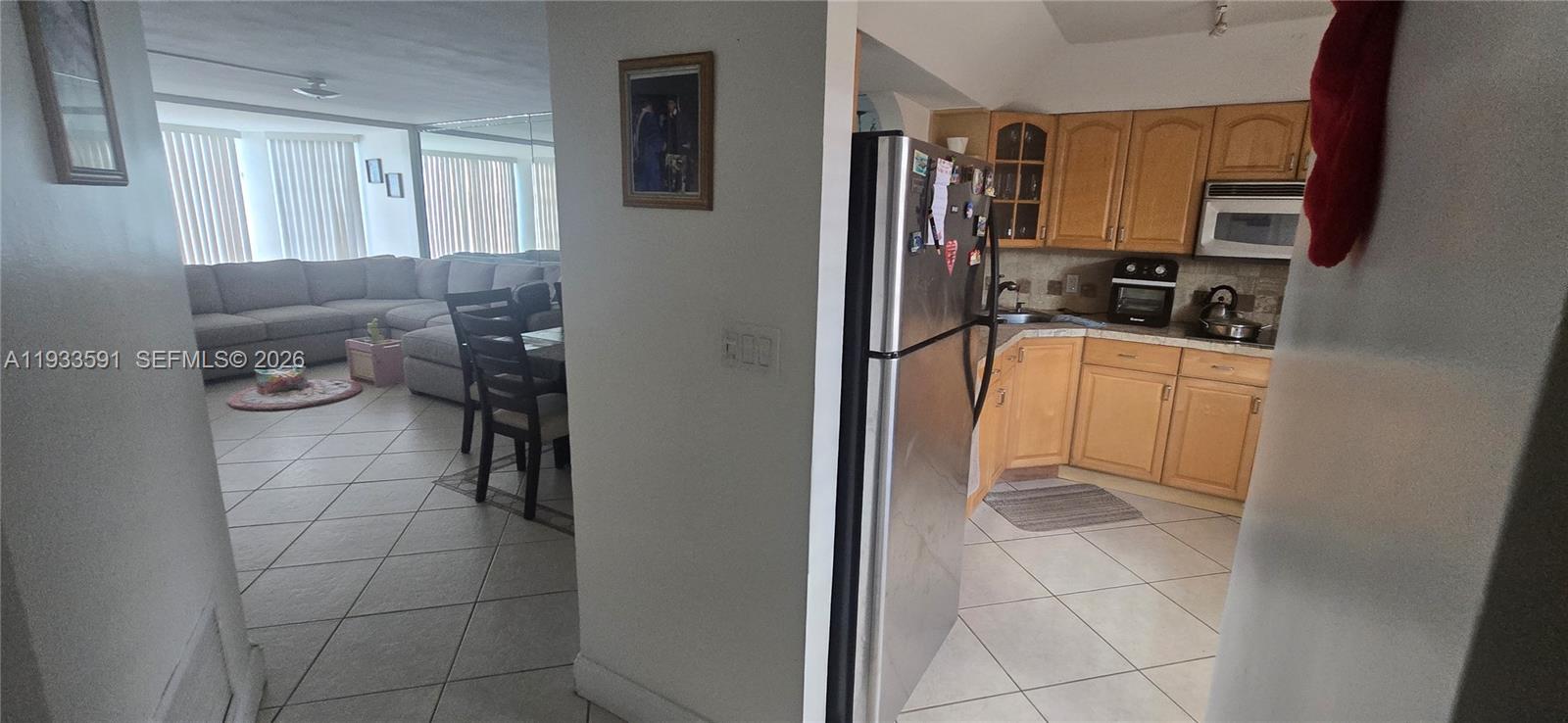 A view from a hallway looking into a kitchen with wood cabinets and a living room — 18900 NE 14th Ave # D105, Miami FL 33179, MIAMI, FL