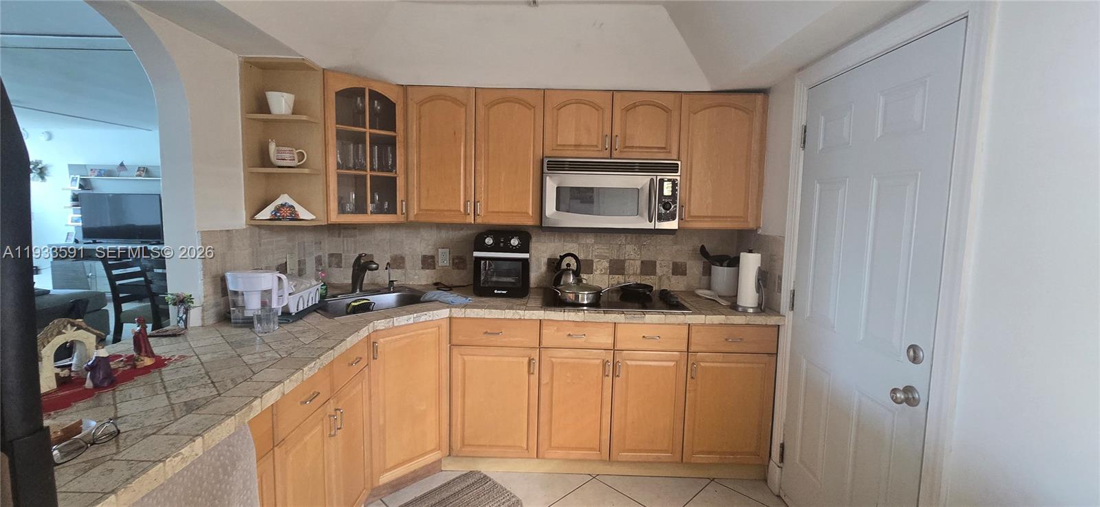 A kitchen features light wood cabinets, tiled countertops, and a stainless steel microwave — 18900 NE 14th Ave # D105, Miami FL 33179, MIAMI, FL