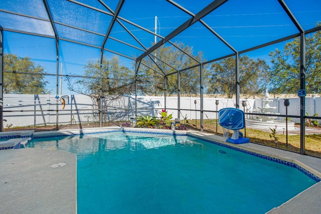 A swimming pool with a basketball hoop is enclosed by a screened lanai in a backyard — 403 CORVINA DRIVE, DAVENPORT, FL