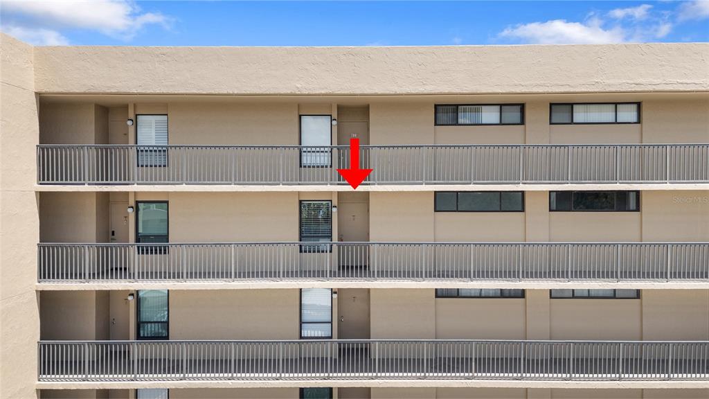 An exterior view of a multi-story apartment building with balconies and a red arrow — 2617 COVE CAY DRIVE UNIT 604, CLEARWATER, FL