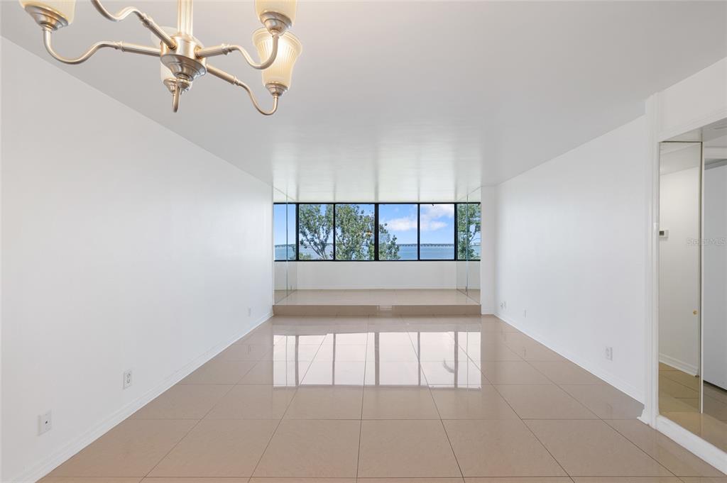 An empty room with beige tile flooring, a chandelier, and a raised windowed seating area — 2617 COVE CAY DRIVE UNIT 604, CLEARWATER, FL
