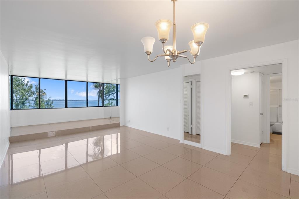 A bright living room features large windows with a water view, tiled floors, and a chandelier — 2617 COVE CAY DRIVE UNIT 604, CLEARWATER, FL