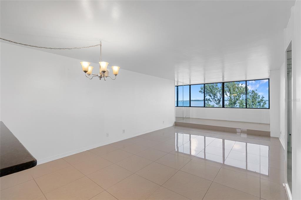 A bright dining area with white walls, tile flooring, a chandelier, and floor-to-ceiling water views — 2617 COVE CAY DRIVE UNIT 604, CLEARWATER, FL