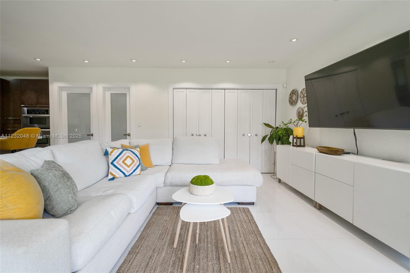 A modern living room features a white sectional sofa, a television, and white cabinetry — 7544 SW 78th Ter, Miami FL 33143, MIAMI, FL