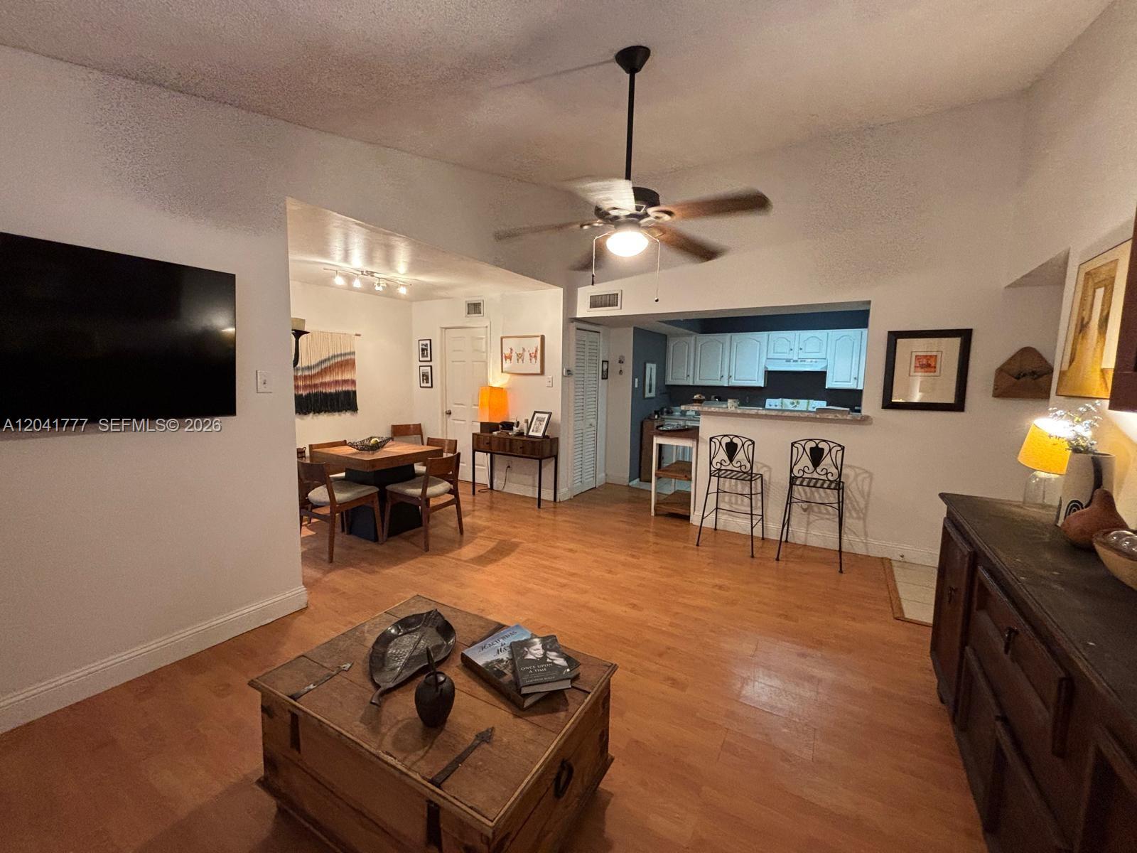 A living room with wood-look flooring, a ceiling fan, and an open view into the kitchen — 15050 SW 103rd Ter # 7202, Miami FL 33196, MIAMI, FL