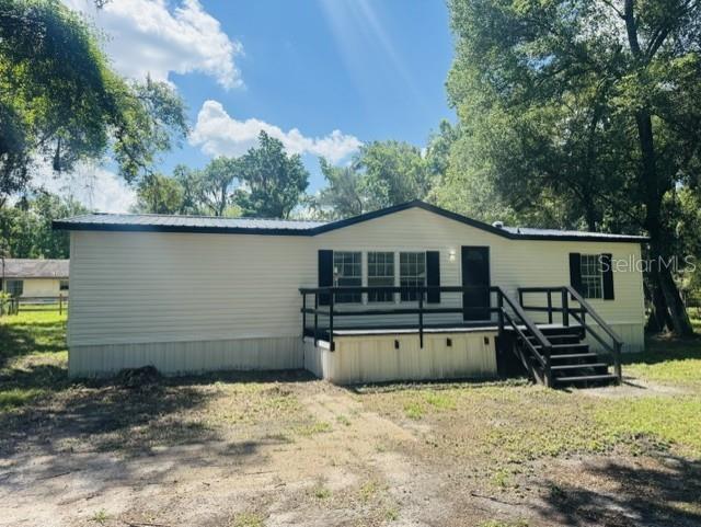 A single-story manufactured home with light siding, a dark metal roof, and a wooden deck — 11898 SW 36TH WAY, WEBSTER, FL