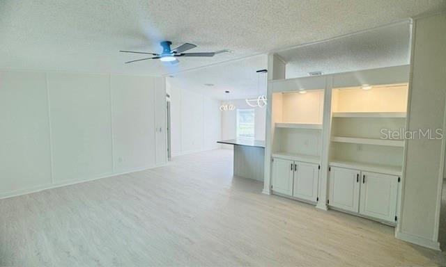 A bright living room features light wood-look flooring, a ceiling fan, and built-in white shelving — 11898 SW 36TH WAY, WEBSTER, FL