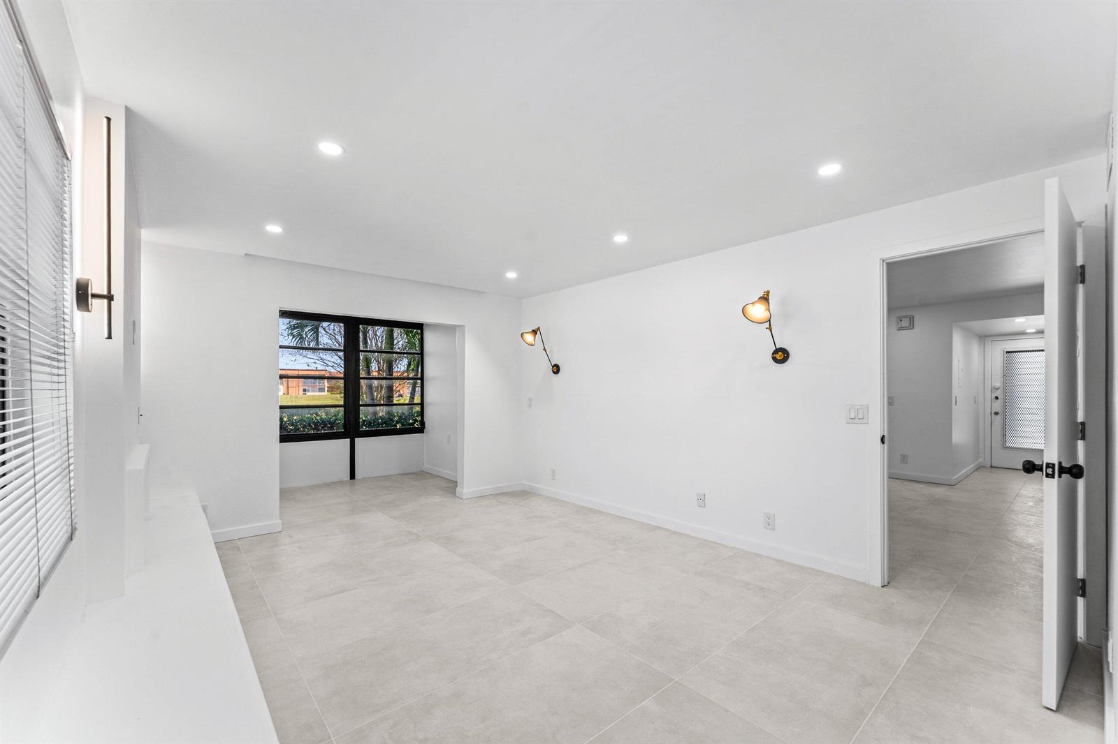 An empty room with white walls, large floor tiles, recessed lighting, and two wall sconces — 551 Piedmont L, Delray Beach FL 33484, DELRAY BEACH, FL