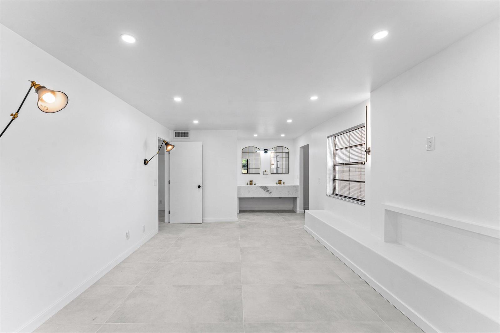 A minimalist bathroom features large gray floor tiles, a double vanity, and white walls — 551 Piedmont L, Delray Beach FL 33484, DELRAY BEACH, FL