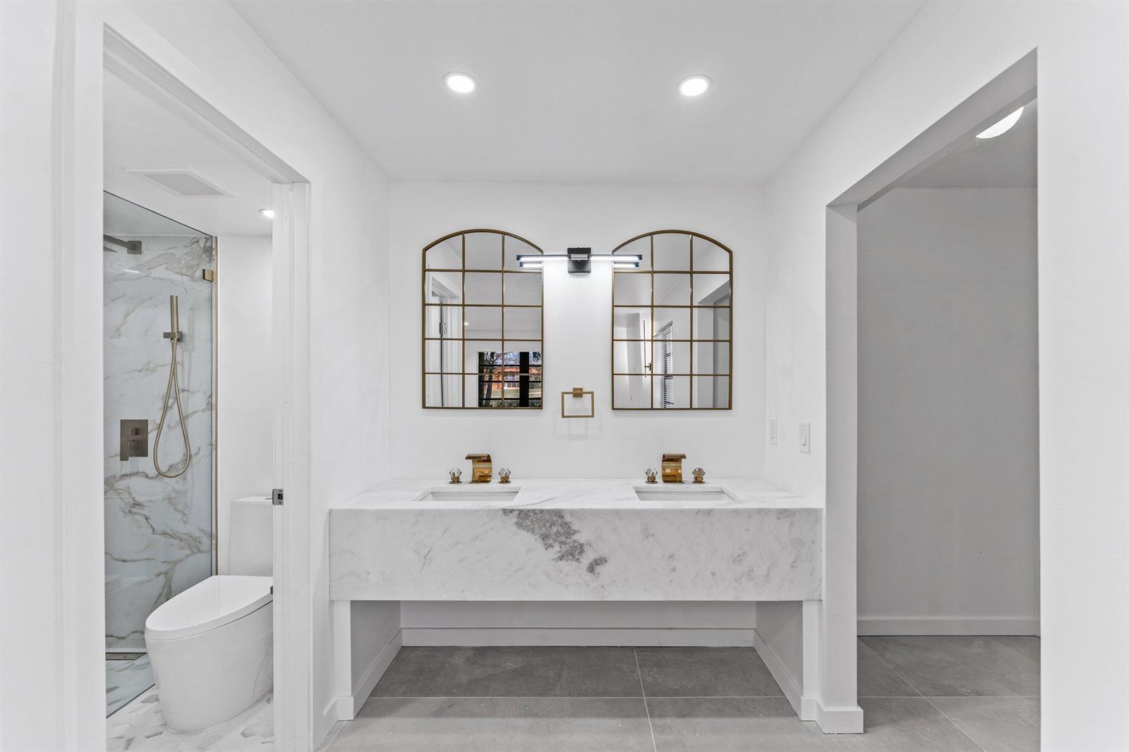 A modern bathroom features a double marble vanity, arched mirrors, and a glass-enclosed shower — 551 Piedmont L, Delray Beach FL 33484, DELRAY BEACH, FL