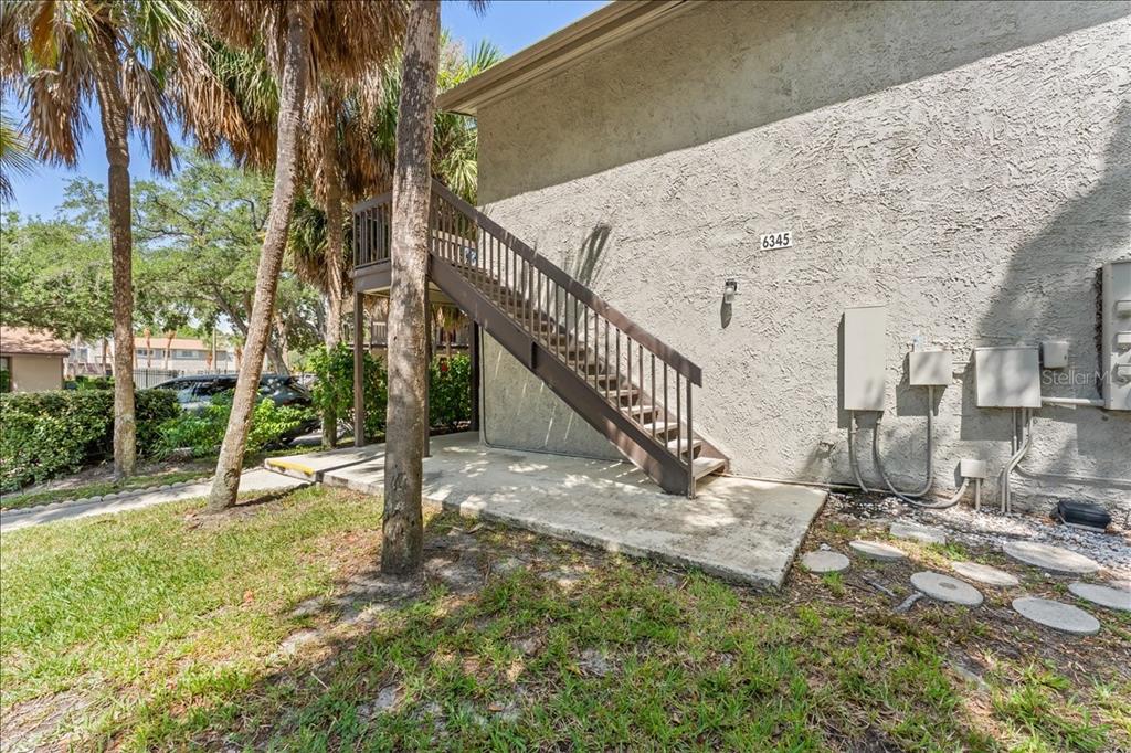 An exterior view of a building with a brown wooden staircase leading to an upper level — 6345 NEWTOWN CIRCLE UNIT 45B2, TAMPA, FL