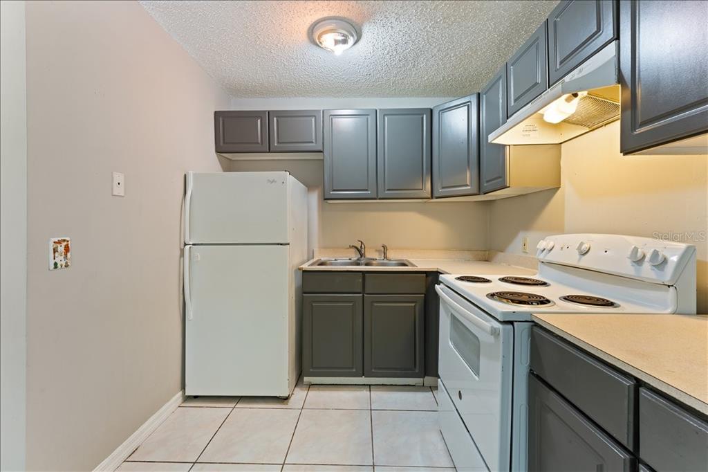 A small kitchen features gray cabinets, white appliances, and light-colored tile flooring — 6345 NEWTOWN CIRCLE UNIT 45B2, TAMPA, FL