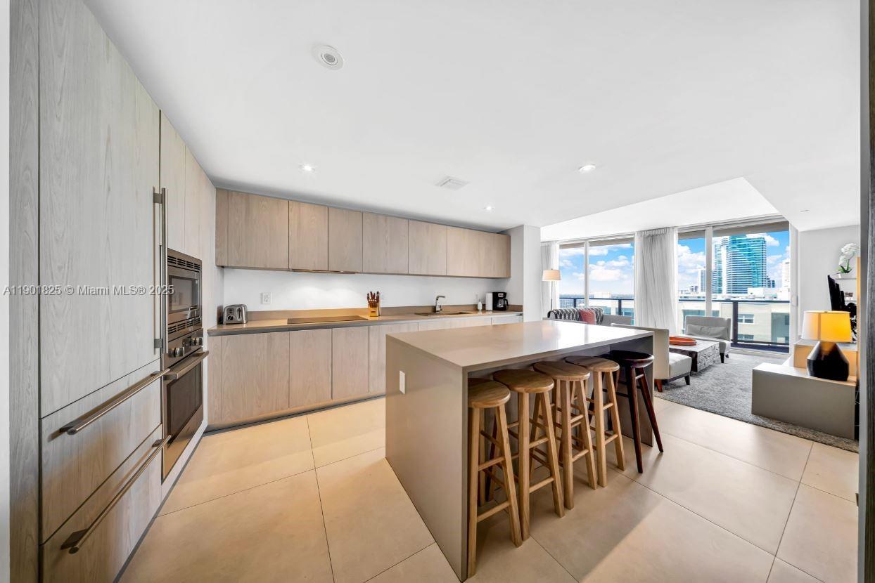 A modern kitchen features light wood cabinetry, a central island with bar stools, and tile flooring — 4111 S Ocean Dr # 1212, Hollywood FL 33019, HOLLYWOOD, FL