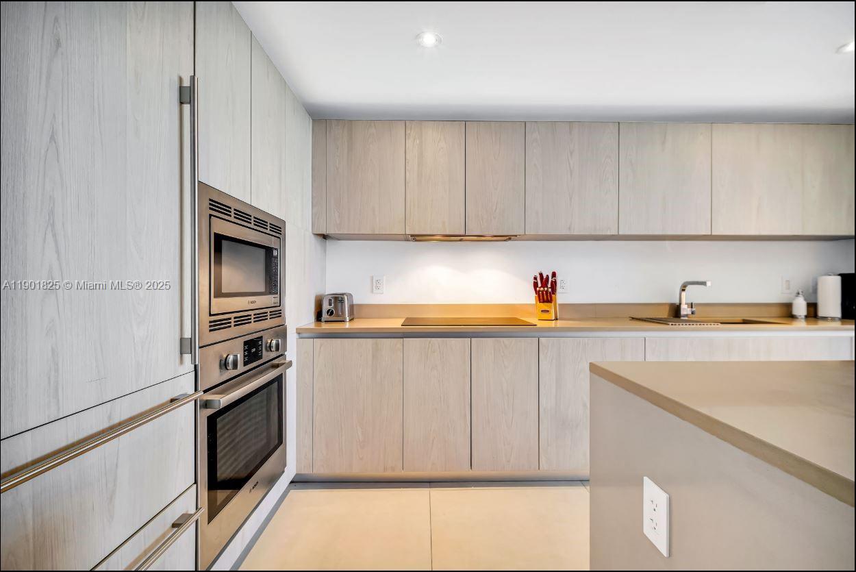 A modern kitchen features light wood cabinetry, stainless steel appliances, and a solid countertop — 4111 S Ocean Dr # 1212, Hollywood FL 33019, HOLLYWOOD, FL