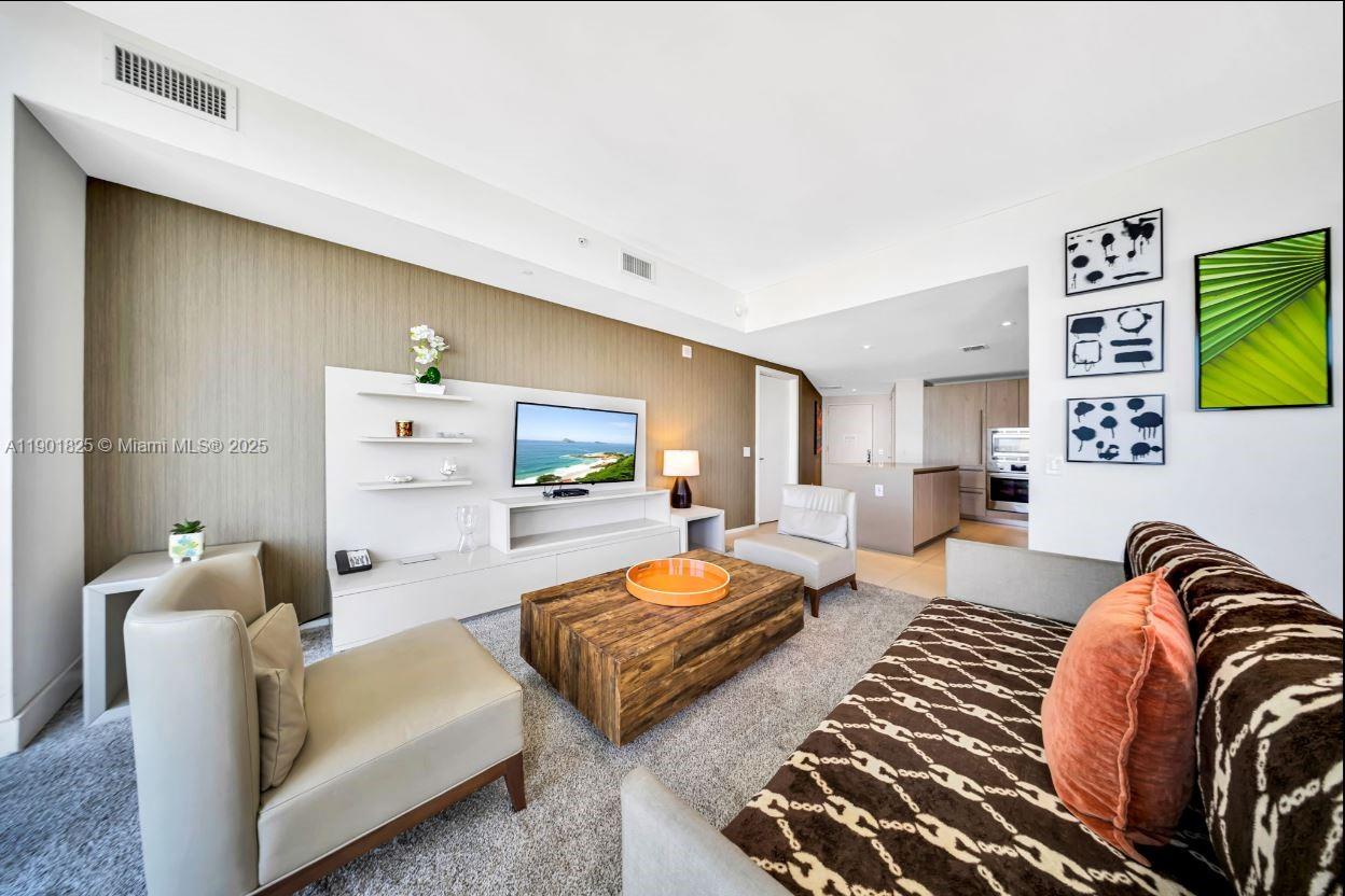 A living room features a wood-paneled wall, a television unit, and patterned sofa seating — 4111 S Ocean Dr # 1212, Hollywood FL 33019, HOLLYWOOD, FL