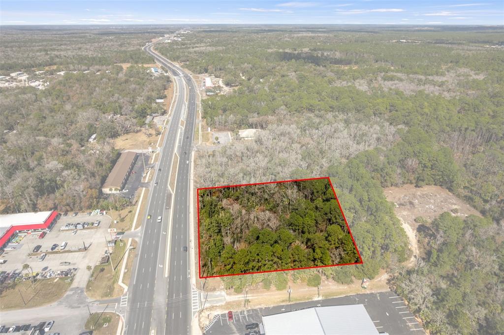 An aerial view shows a rectangular wooded lot outlined in red next to a highway — 8541 W FAUST LANE, HOMOSASSA, FL