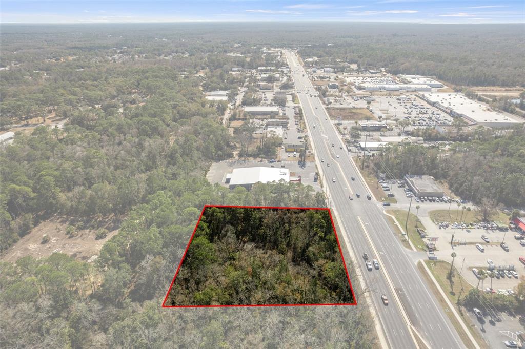 An aerial view shows a wooded lot outlined in red next to a busy highway — 8541 W FAUST LANE, HOMOSASSA, FL