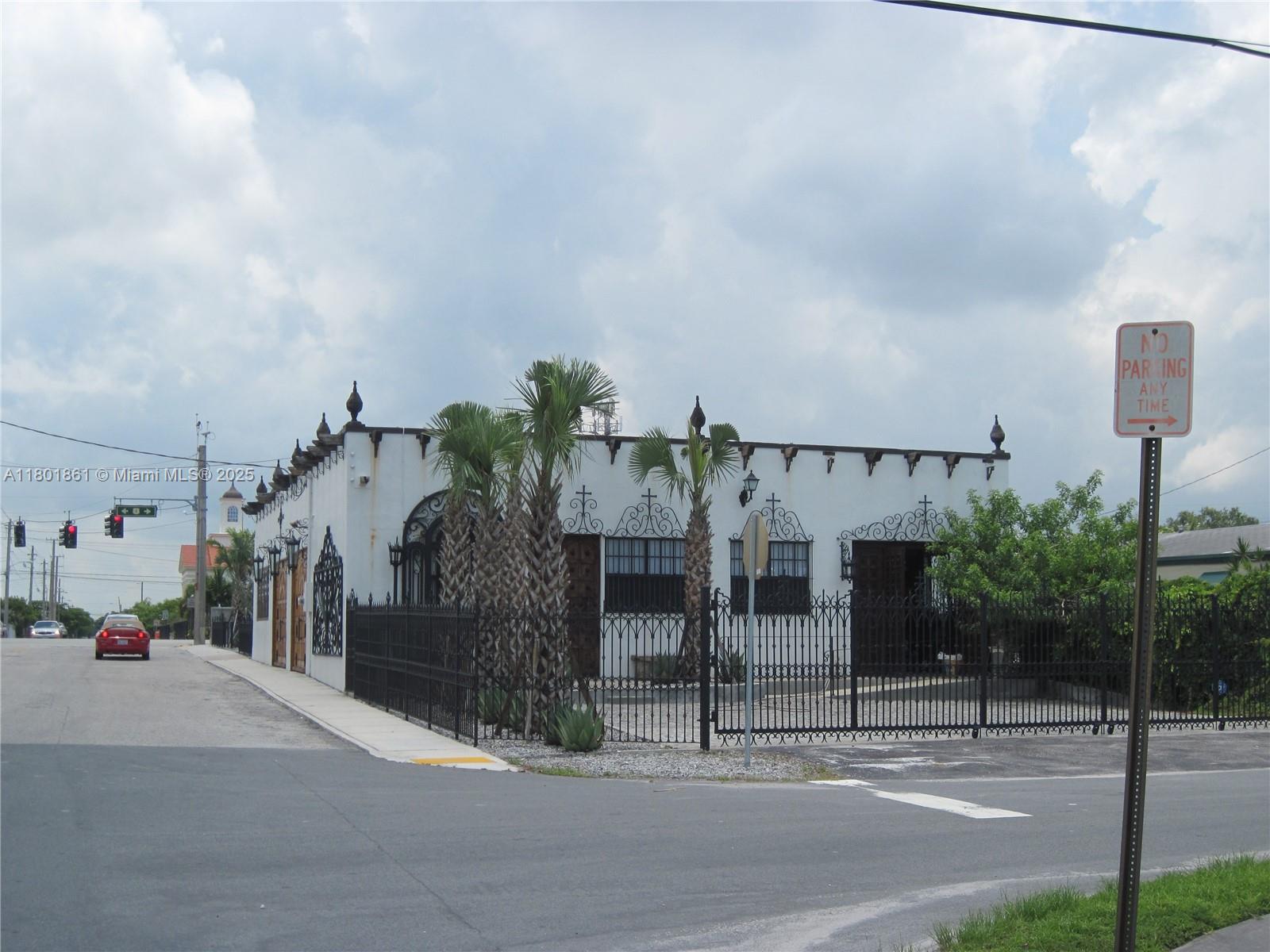 A white building with decorative ironwork and palm trees stands behind a black metal fence — 101 NE 1st St, Dania Beach FL 33004, DANIA BEACH, FL