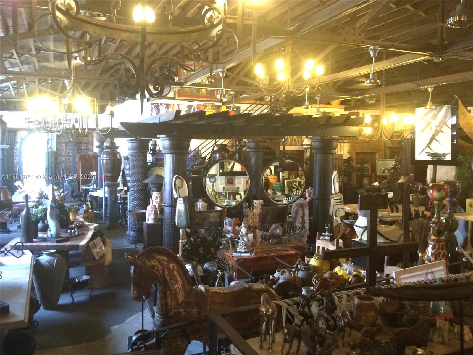 A cluttered antique shop interior features wooden pillars, hanging chandeliers, and various decorative objects — 101 NE 1st St, Dania Beach FL 33004, DANIA BEACH, FL