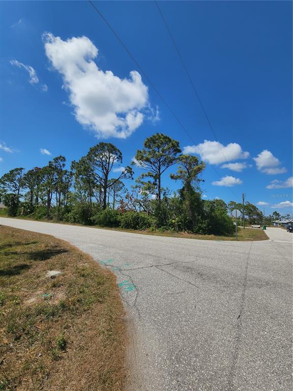A paved road curves past a vacant, tree-lined lot under a blue sky — 12282 APPLEBERG CIRCLE, PORT CHARLOTTE, FL