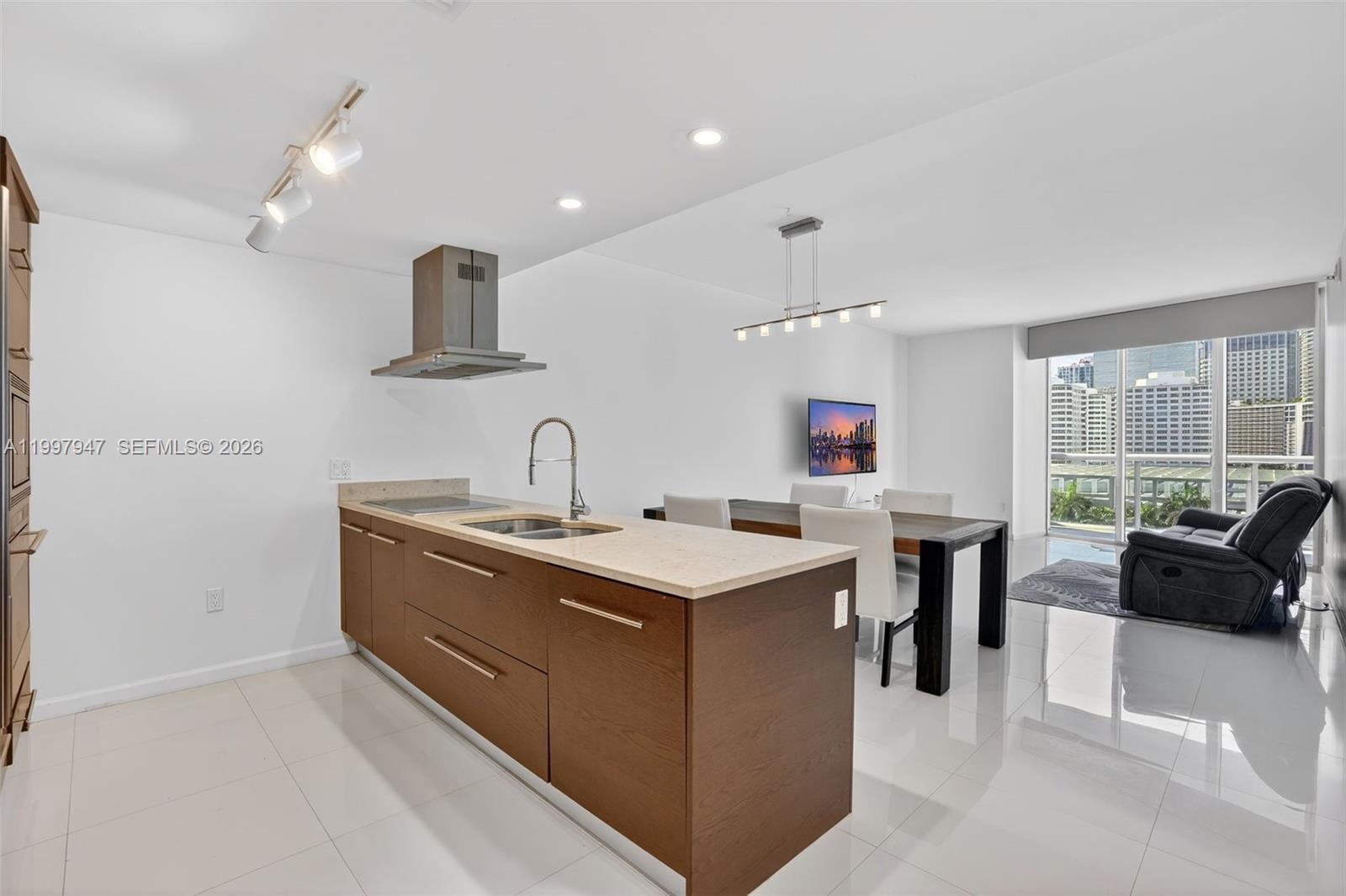 A modern kitchen with wood cabinets and a stone island overlooks a dining area — 495 Brickell Ave # 1007, Miami FL 33131, MIAMI, FL