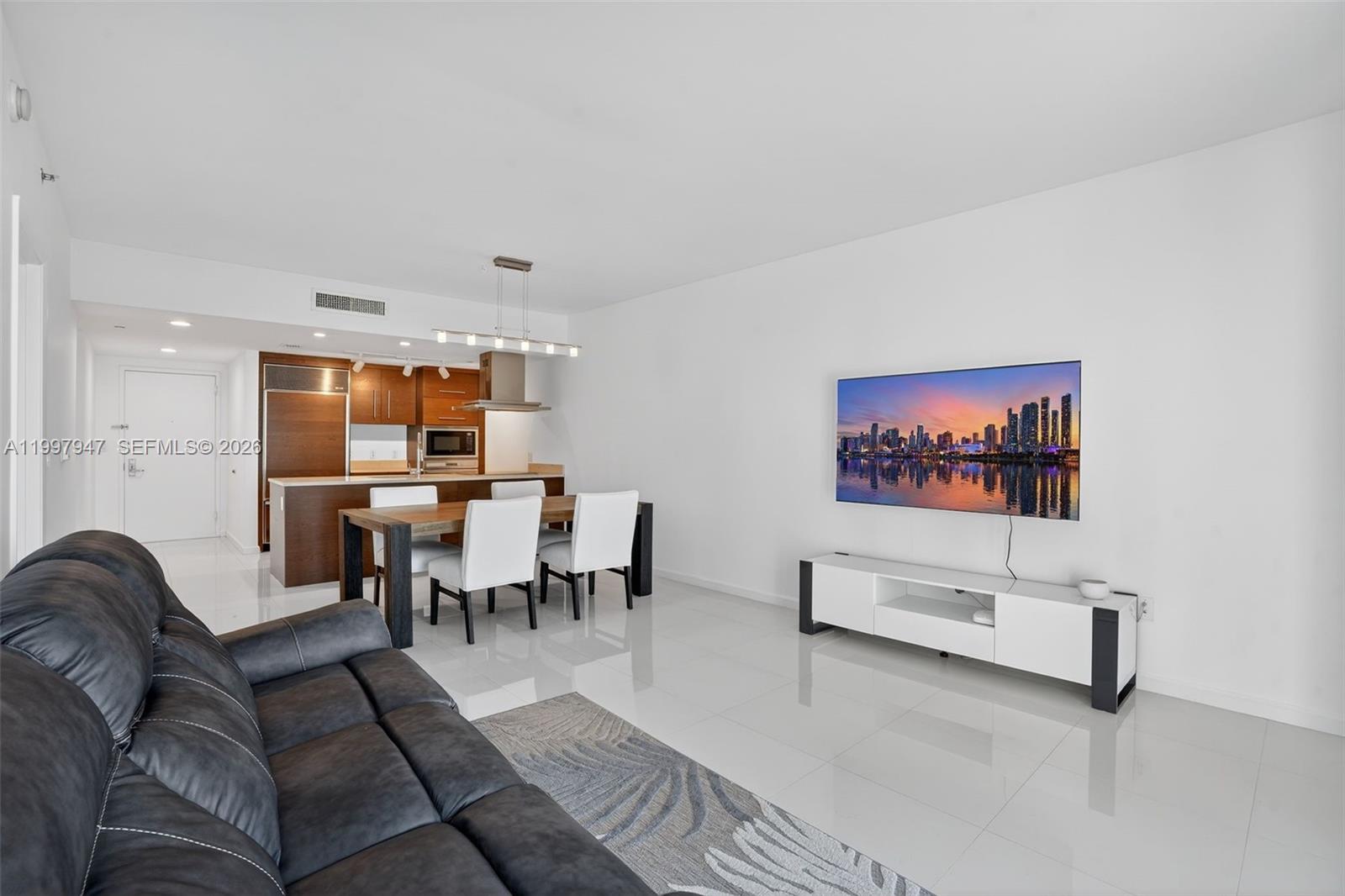 A modern living and dining area features white tile floors, a dark sofa, and a television — 495 Brickell Ave # 1007, Miami FL 33131, MIAMI, FL