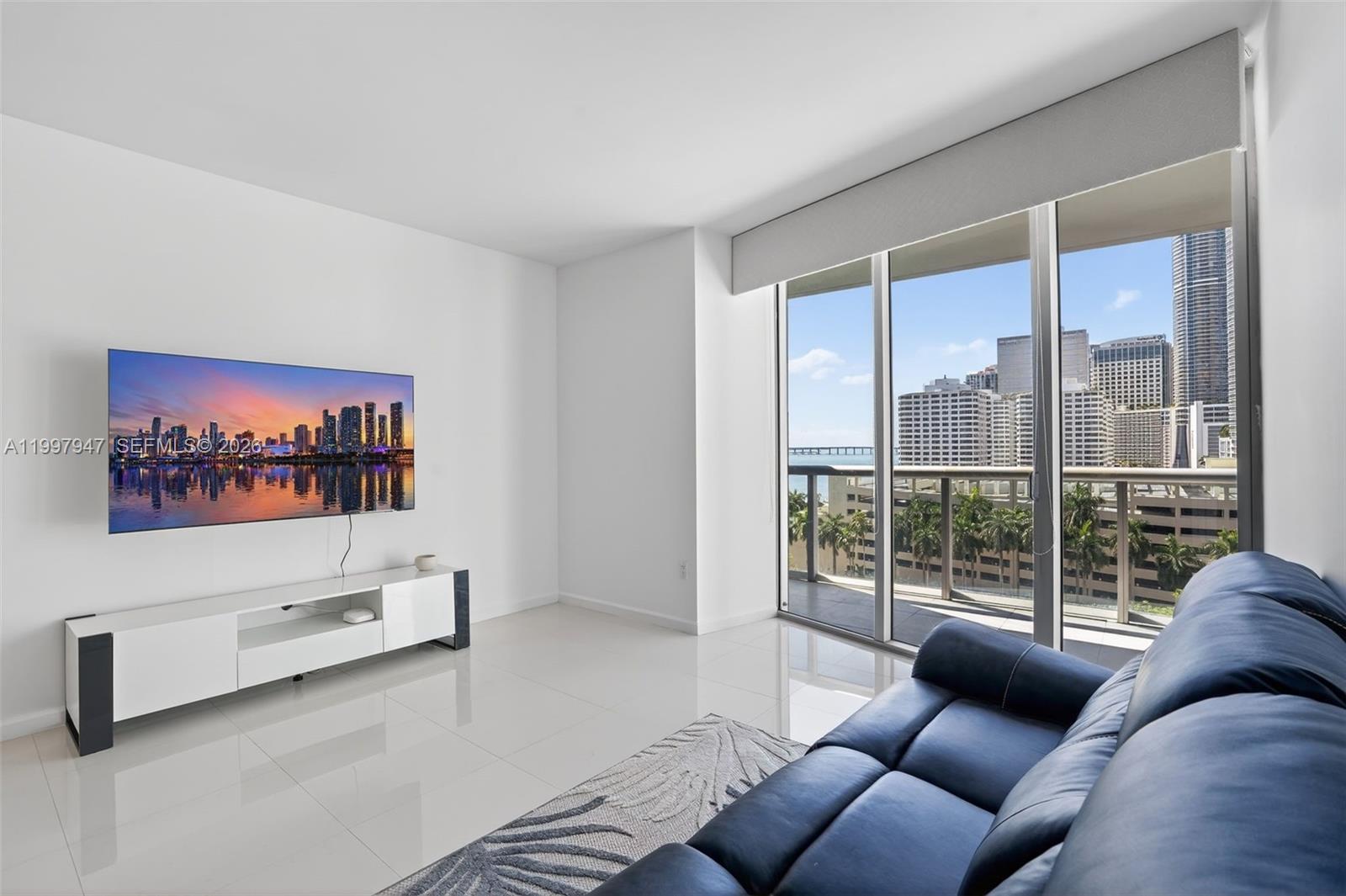 A living room features white tile floors, a blue leather sofa, and a balcony view — 495 Brickell Ave # 1007, Miami FL 33131, MIAMI, FL