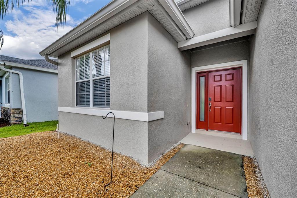 A gray stucco house exterior features a red front door and a gravel front yard — 2628 BALFORN TOWER WAY, WINTER GARDEN, FL