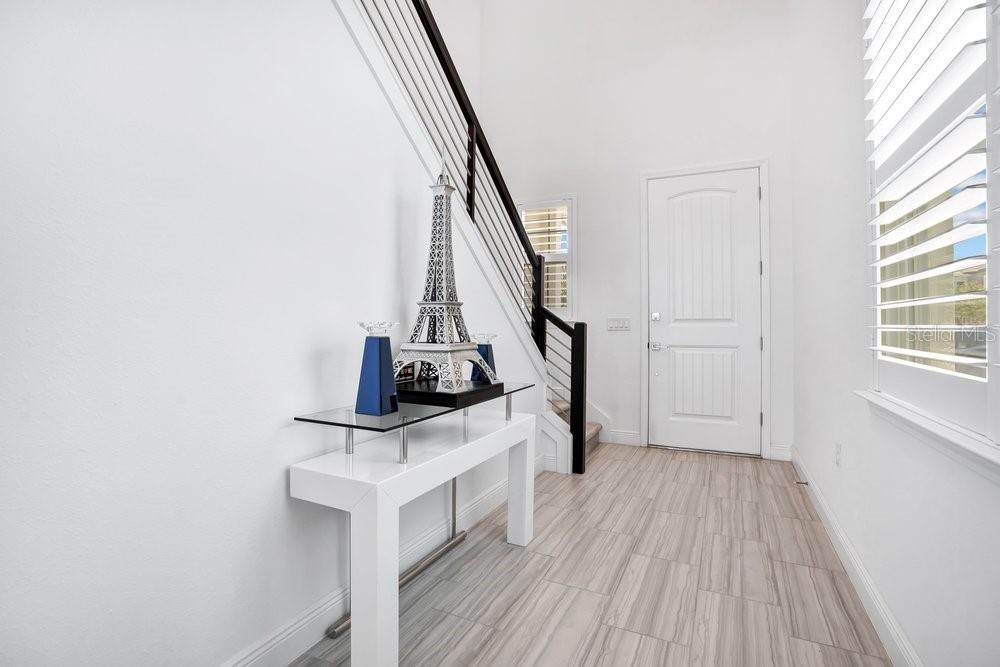 A bright entryway features a white console table, a model Eiffel Tower, and a staircase — 15738 VETTA DRIVE, BELLA COLLINA, FL
