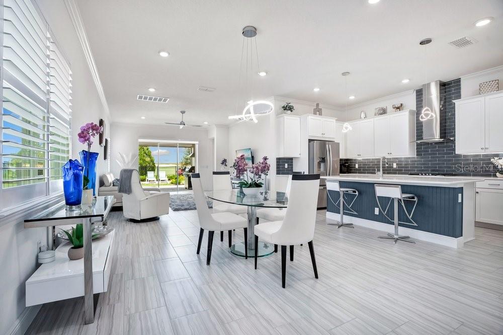 A bright, open-concept kitchen and dining area featuring white cabinetry, a blue island, and tile flooring — 15738 VETTA DRIVE, BELLA COLLINA, FL
