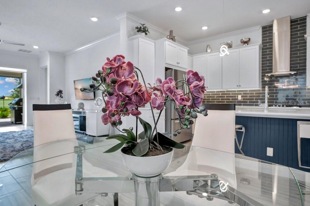 A dining area features a glass table with a purple orchid centerpiece and white chairs — 15738 VETTA DRIVE, BELLA COLLINA, FL