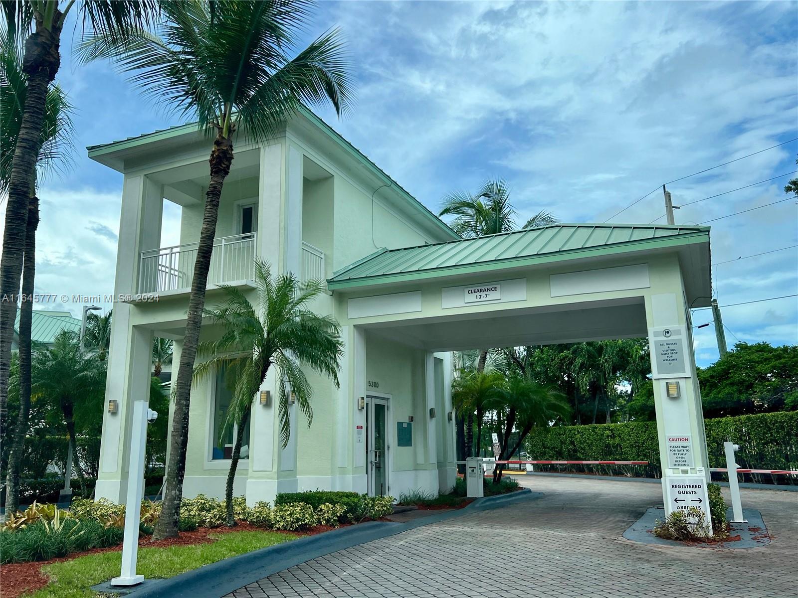 A gated entrance features a light green building with a covered driveway and palm trees — 5300 NW 87th Ave # 1308, Doral FL 33178, DORAL, FL