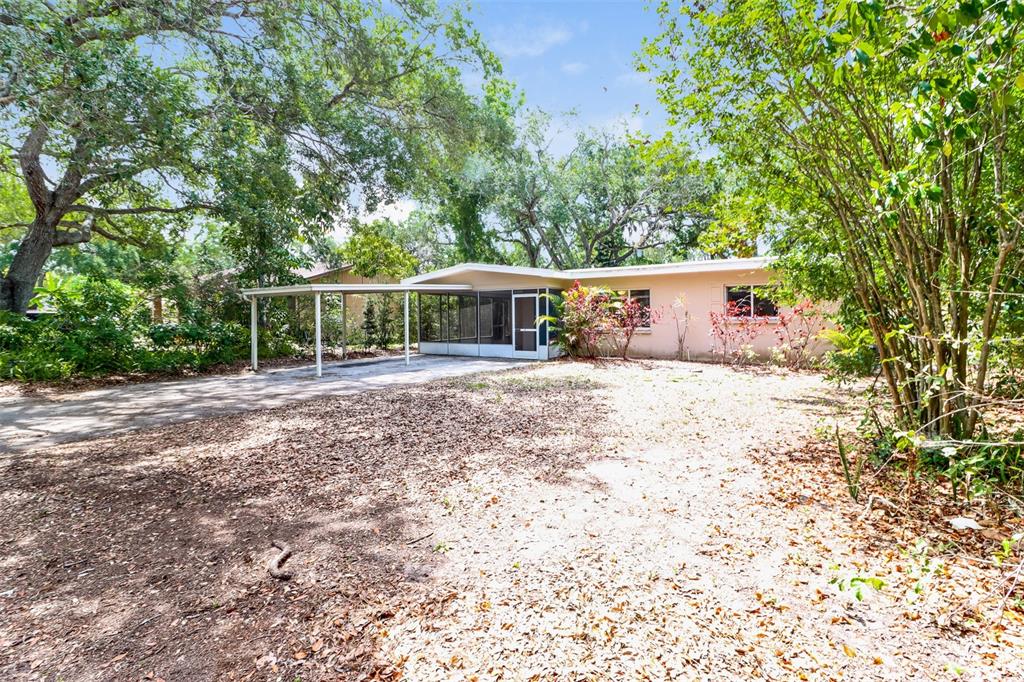 A single-story house with a carport and a screened-in porch sits on a wooded lot — 1619 EDNA AVENUE, LARGO, FL