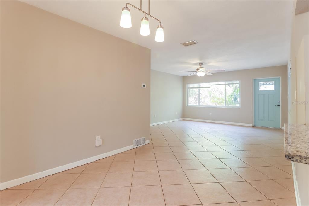 An open-concept living and dining area features beige walls, tile flooring, and a light-blue door — 1619 EDNA AVENUE, LARGO, FL
