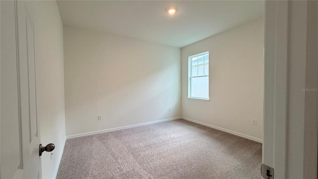An empty bedroom features beige walls, neutral carpeting, a single window, and a ceiling light — 2334 SELENIA STREET, LAKE ALFRED, FL