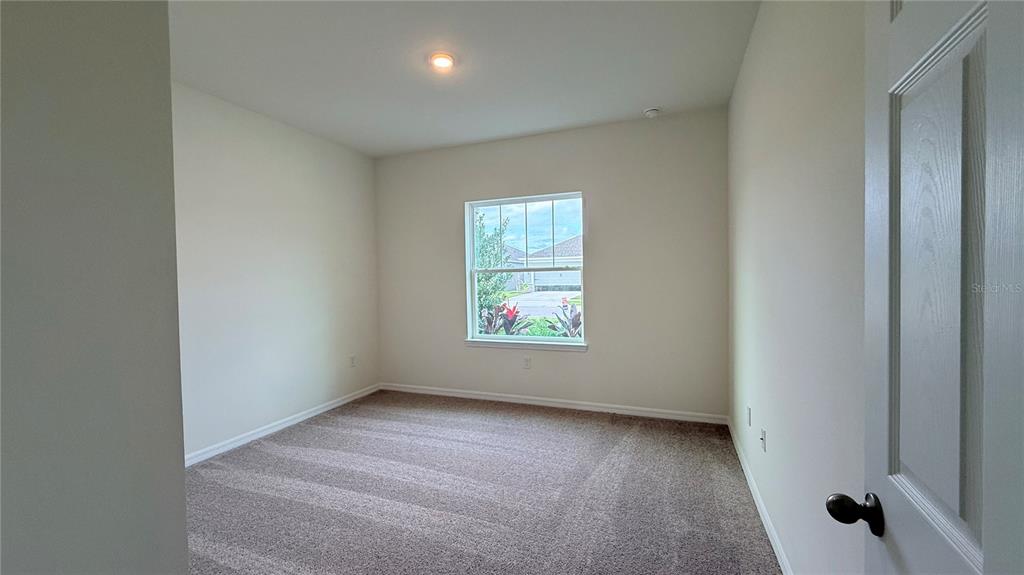 An empty bedroom features beige walls, neutral carpeting, and a single window overlooking a neighborhood — 2334 SELENIA STREET, LAKE ALFRED, FL
