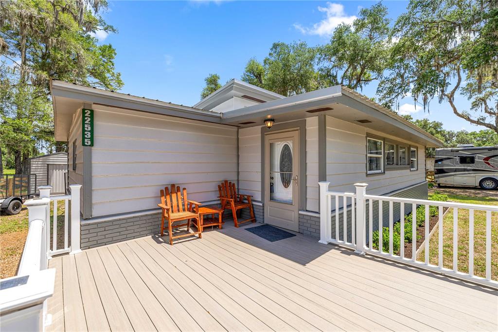 A light-colored house exterior features a wooden deck, white railings, and two wooden chairs — 22535 SW 117TH STREET, DUNNELLON, FL