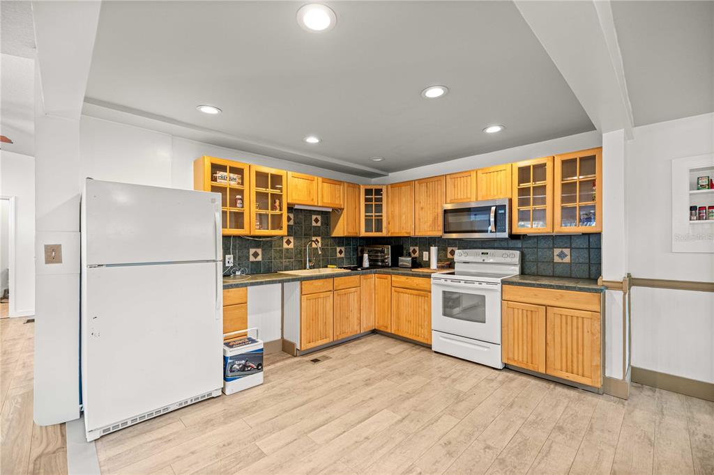 A kitchen features light wood cabinets, dark tile backsplashes, white appliances, and light wood flooring — 22535 SW 117TH STREET, DUNNELLON, FL