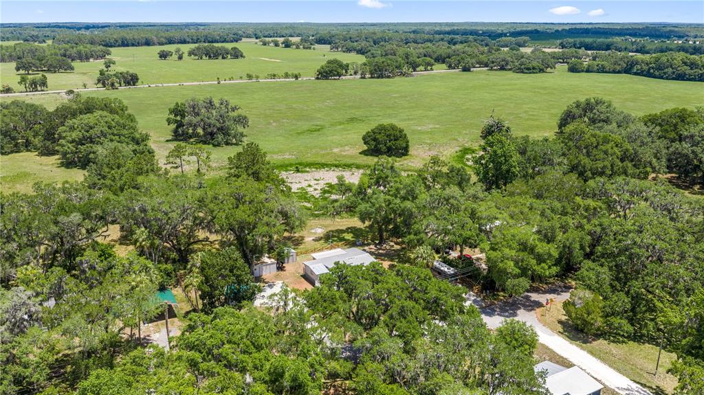 An aerial view shows a house nestled among trees surrounded by large, open green pastures — 22535 SW 117TH STREET, DUNNELLON, FL